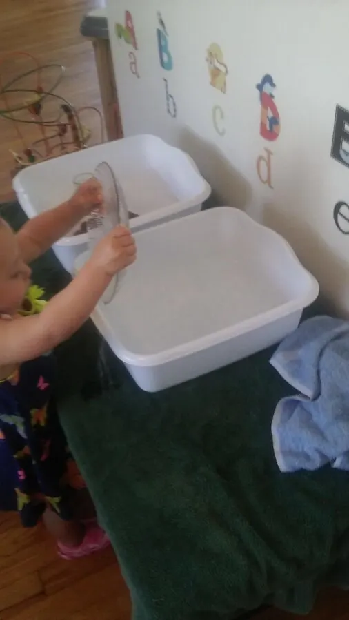 close up of dishwashing station for child and child washing a glass plate.