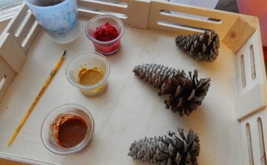 paints mixed with spices, 3 pinecones, paintbrush on wooden tray for Spice Painting Fall activity.