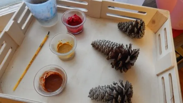 paints mixed with spices, 3 pinecones, paintbrush on wooden tray for Spice Painting Fall activity.