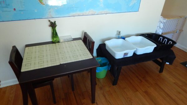 A child's table, next to a dishwashing station for child.