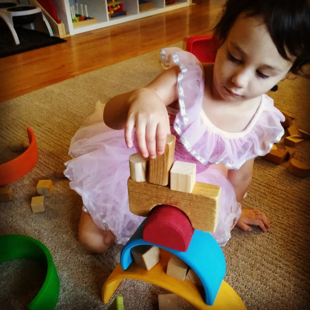 child stacking wooden blocks with Grimm's rainbow pieces.