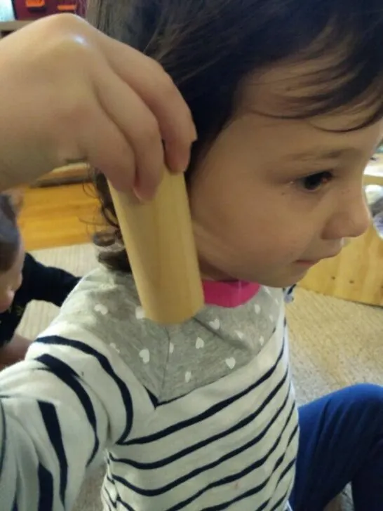 child holding montessori sensory material, sound cylinders.