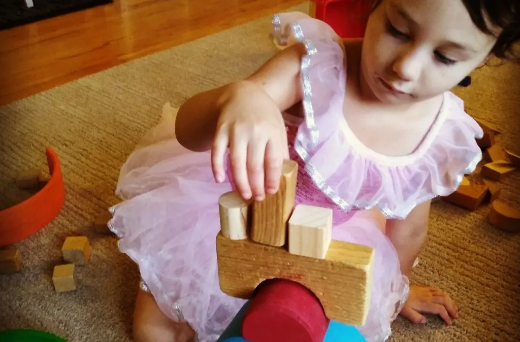 child doing loose parts play by stacking wooden blocks with grimm's rainbow pieces.