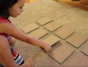 sandpaper numbers face down on ground, child about to flip one over during the zero game.
