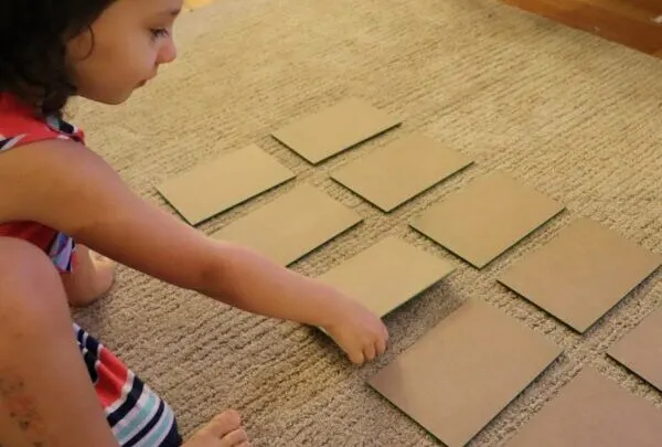 image of sandpaper numbers face down on ground, child about to flip one over during the zero game.