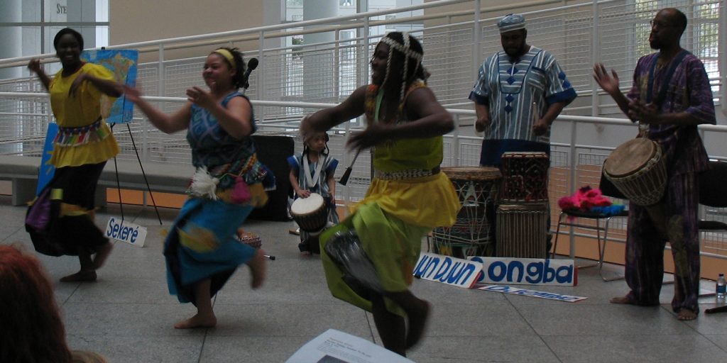 People dancing with people using drums behind them. Use music to teach your child about their cultural heritage.