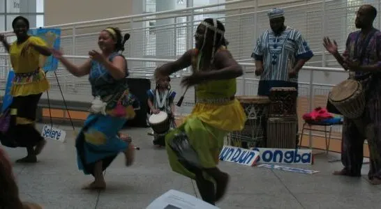 People dancing with people using drums behind them. Use music to teach your child about their cultural heritage.