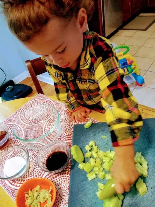 Toddler cutting up vegetables using a wavy chopper.