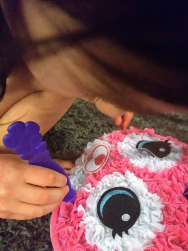 Child pushing pieces of fabric into Cat Pillow Plush Craft Kit using her pincer grasp.