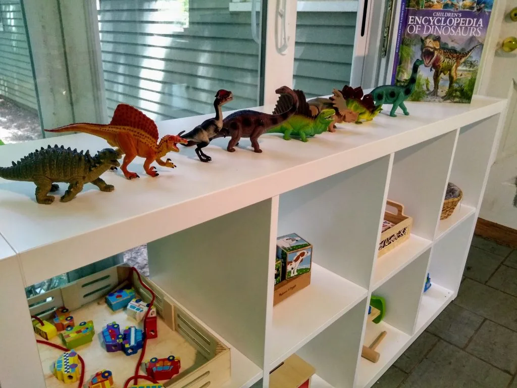 "How To Organize Playroom" image of shelf full of wooden and dinosaur toys.