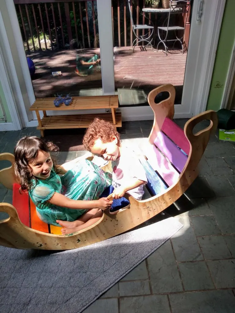 brother and sister playing on a rainbow wooden rocker.