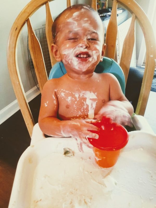 baby covered in food in booster chair, why messy play is important.
