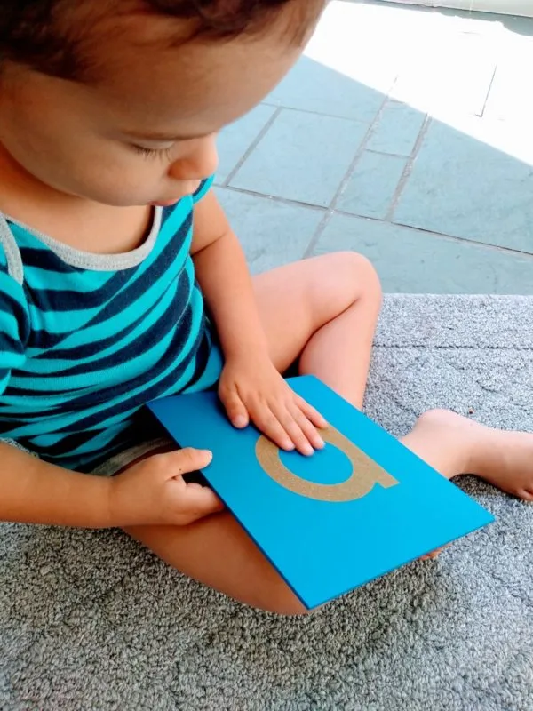 Young boy feeling Sandpaper Letter. Part of a fun Montessori sound game. Used in the sensitive periods for sensation and language/reading/writing.