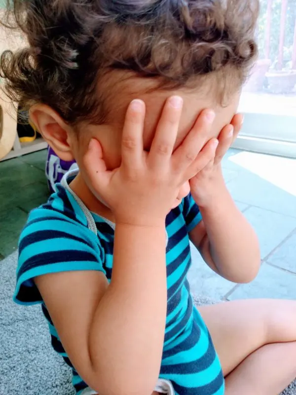 Young child covering his eyes, playing a Montessori sound game.