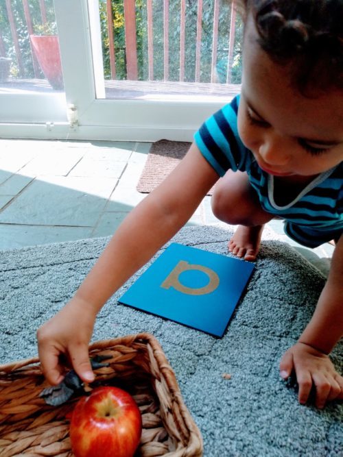 A young child using Sandpaper Letters and small objects to play a Montessori sound game.