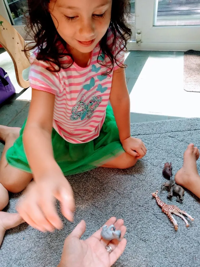 Girl playing Montessori sound games by finding small animals with certain letter sounds and handing them to her mom.