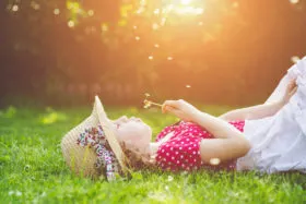 child laying in the grass, blowing dandelion, 