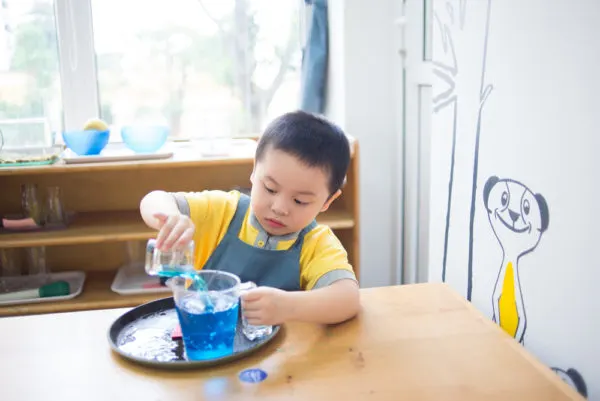 child pouring water from small glass to large glass