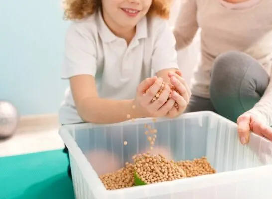 Child playing with beans in sensory bin during sensory integration therapy.