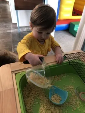 toddler pouring cereal in sensory play table.