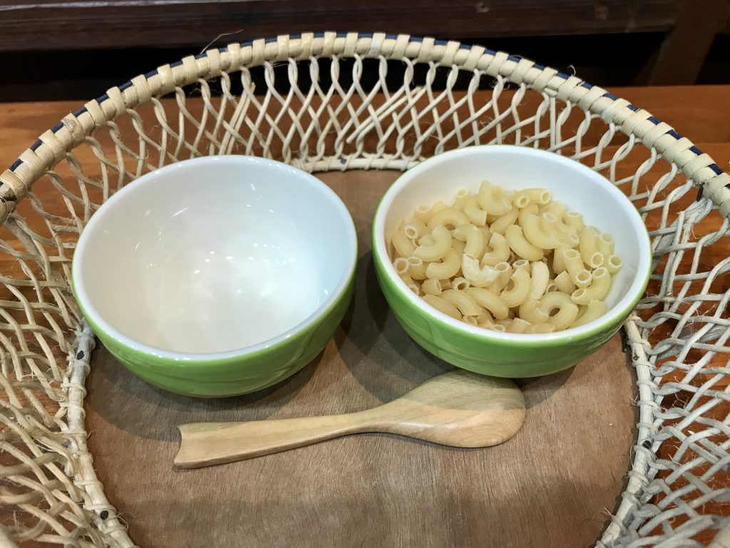 Montessori practical life activity, two bowls, one empty, one with macaronis and a spoon for scooping.
