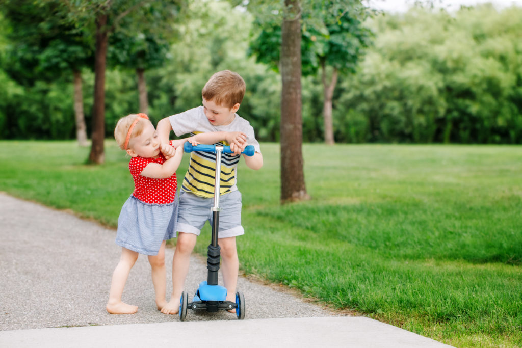 "Teach Kids How To Share" image of two kids fighting over a scooter.