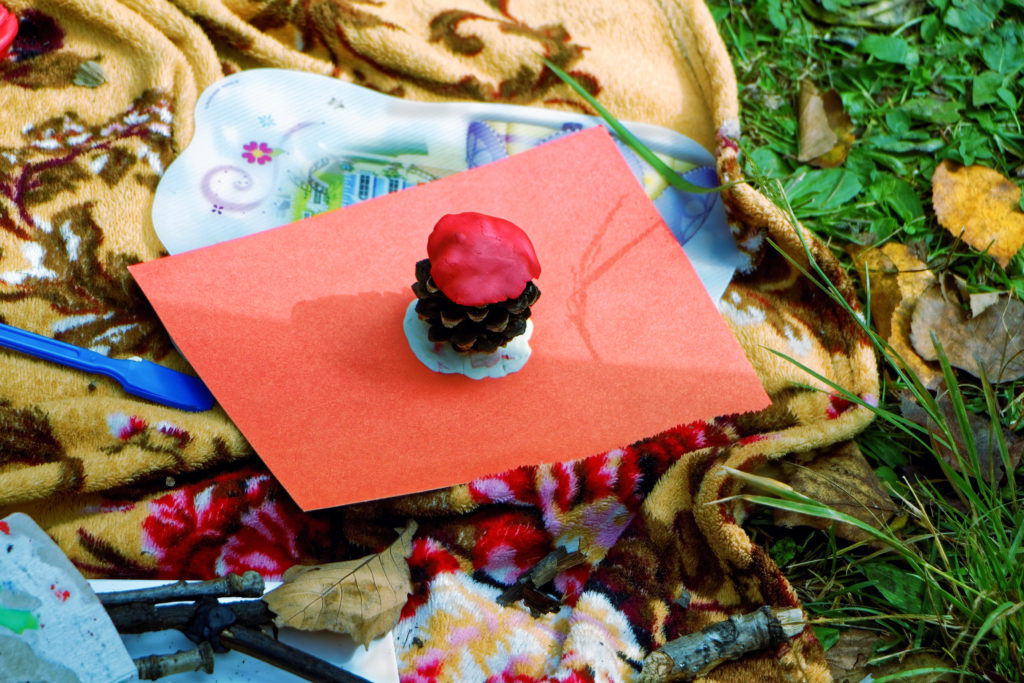 loose parts play image of pinecone, playdoh and glue on piece of red paper.