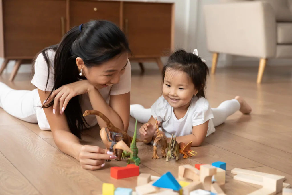 Mother and child playing with dinosaur gifts on the floor.