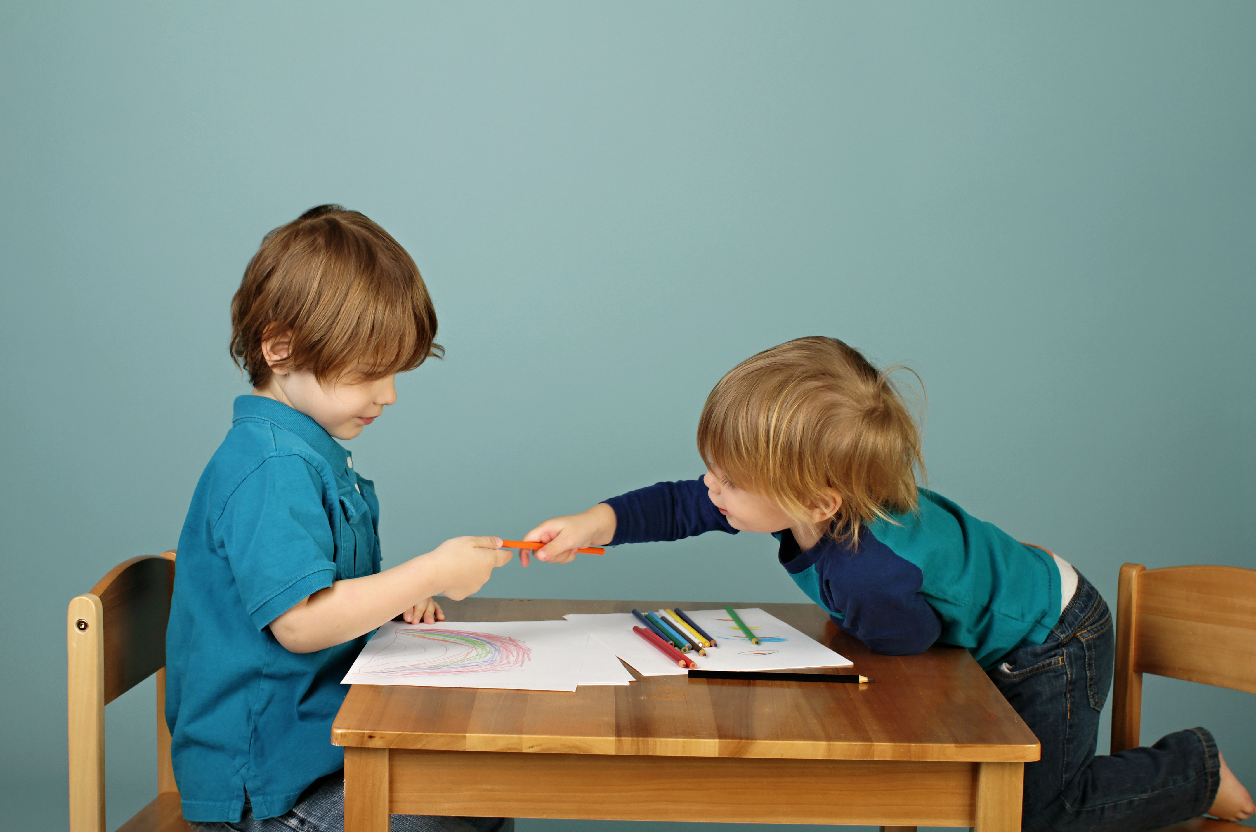 Teach Kids How To Share image of two boys sharing colored pencils while drawing.