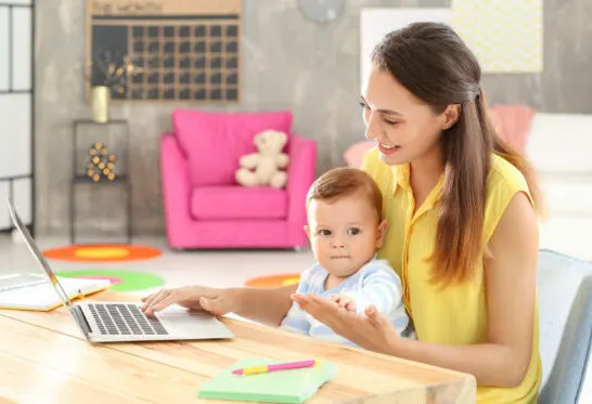 Woman with baby on lap, looking through Montessori blogs.