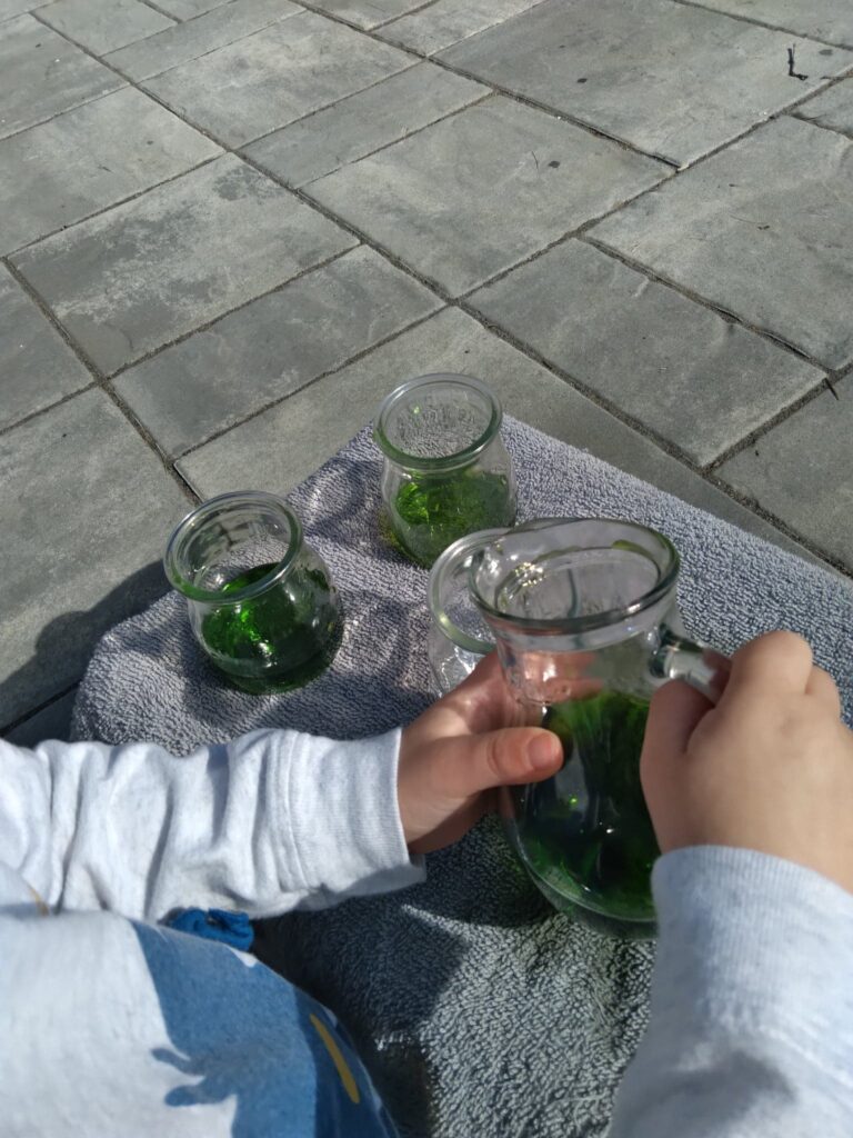 child pouring water from glass pitcher to glasses.