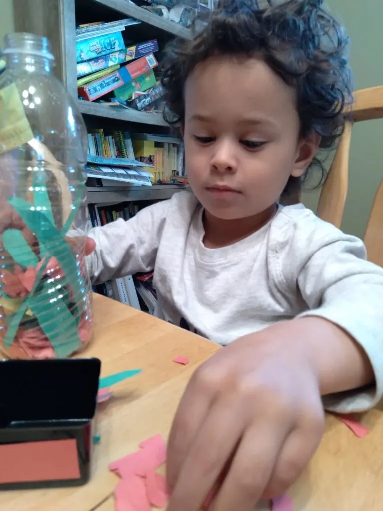 child tearing bits of paper and putting them in a bottle.