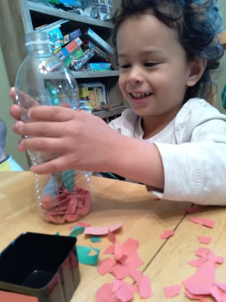 child smiling and looking at bottle of torn paper.