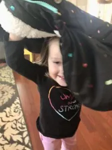 Toddler proudly learning how to put on a coat, by flipping it over their head.