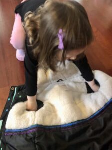 toddler learning how to put on a coat by putting arms through sleeves, coat is on ground upside down.