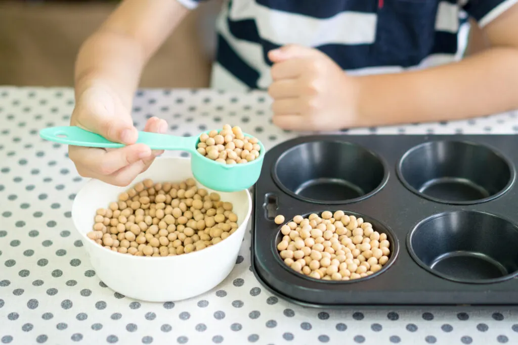 child spooning beans from bowl to muffin tin.