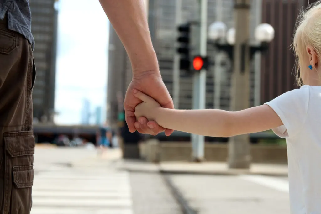 child holding father's hand while crossing the street.