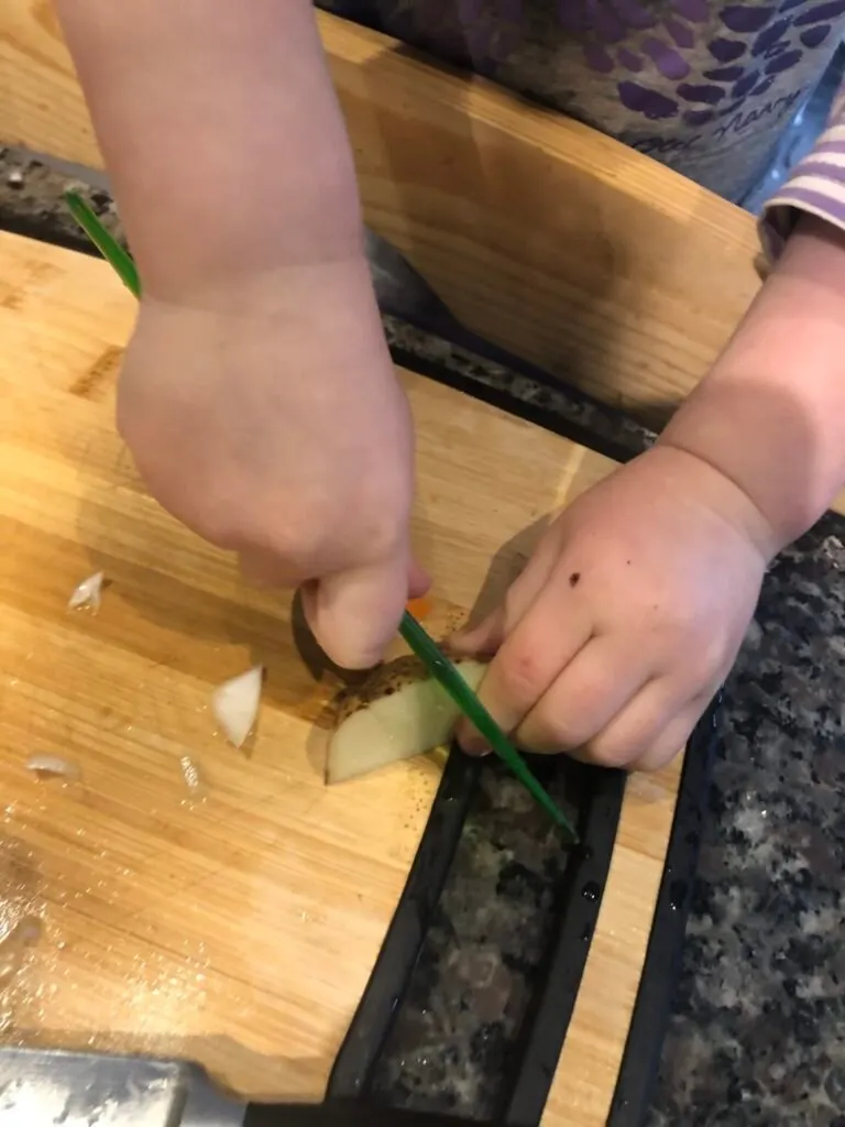 Toddler using plastic knife to cut potatoes for soup.