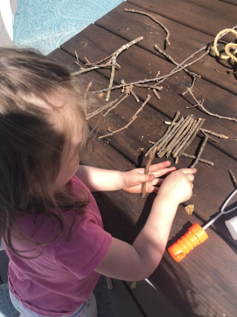 toddler putting together stick raft.