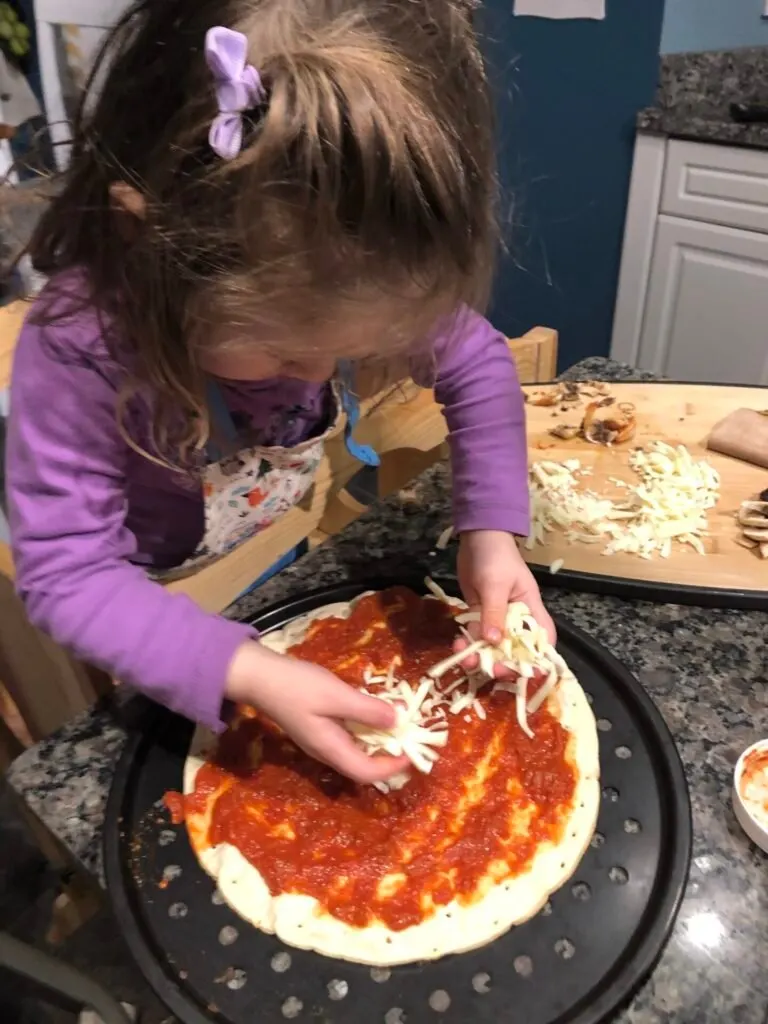 Toddler putting mozzarella on pizza.