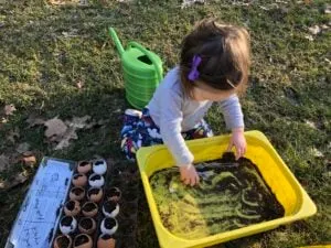 toddler planting seeds in eggshells for a Montessori outdoor activity.