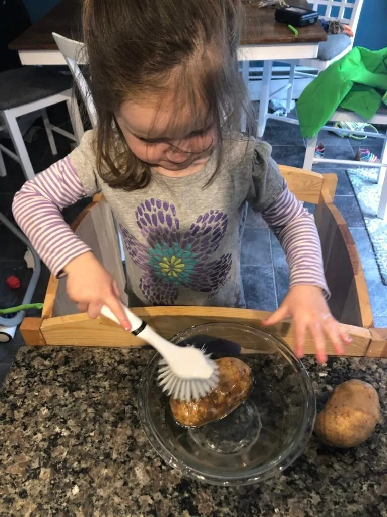 Toddler scrubbing potatoes.
