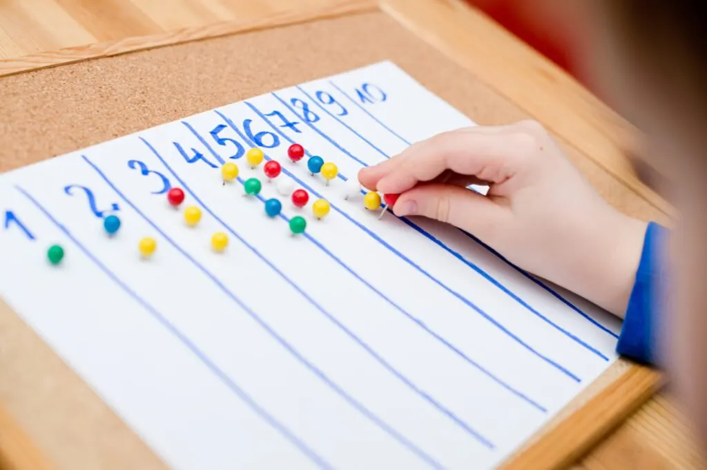 child using push pins for 1:1 correspondence Montessori math activity.