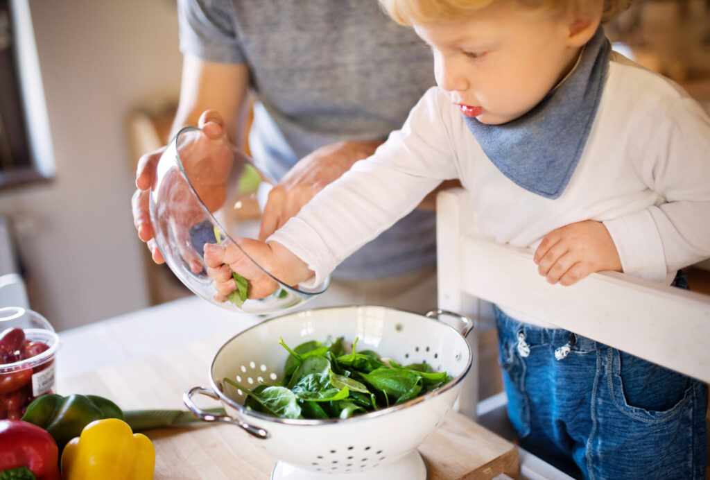 child on Montessori learning tower, cooking with parent.