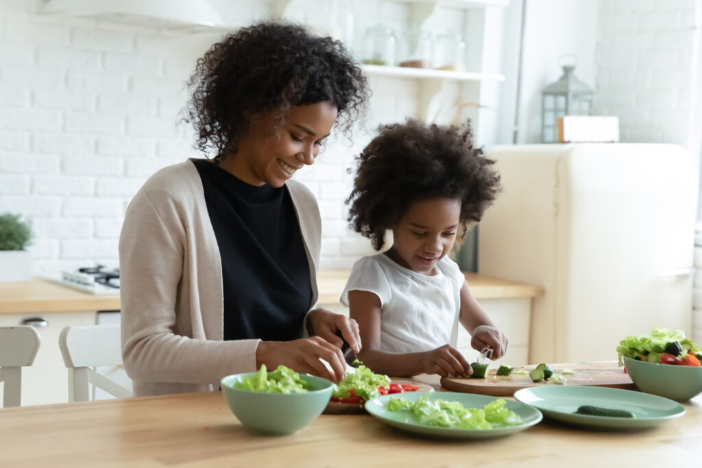 image of child using Montessori knife with mother. Cutting vegetables in the kitchen.