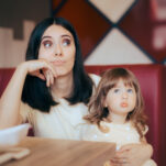 bored child without toys at restaurant, sitting on stressed mother's lap.