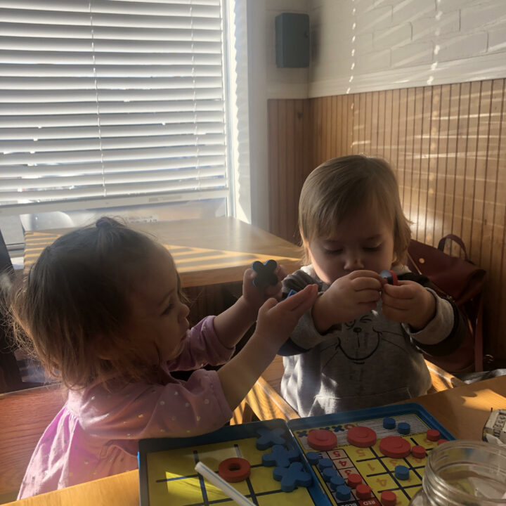 toys at restaurants: two toddlers playing with tic tac toe game at table.