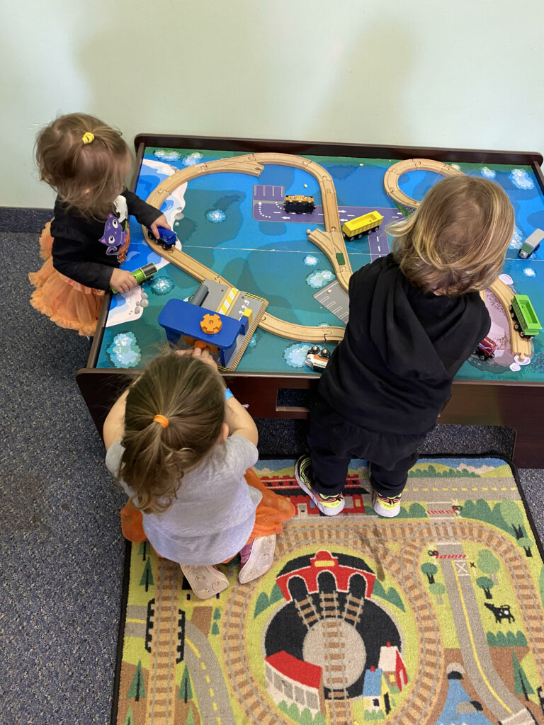 3 toddlers playing at train table, demonstrating parallel play, one of the 6 stages of play.