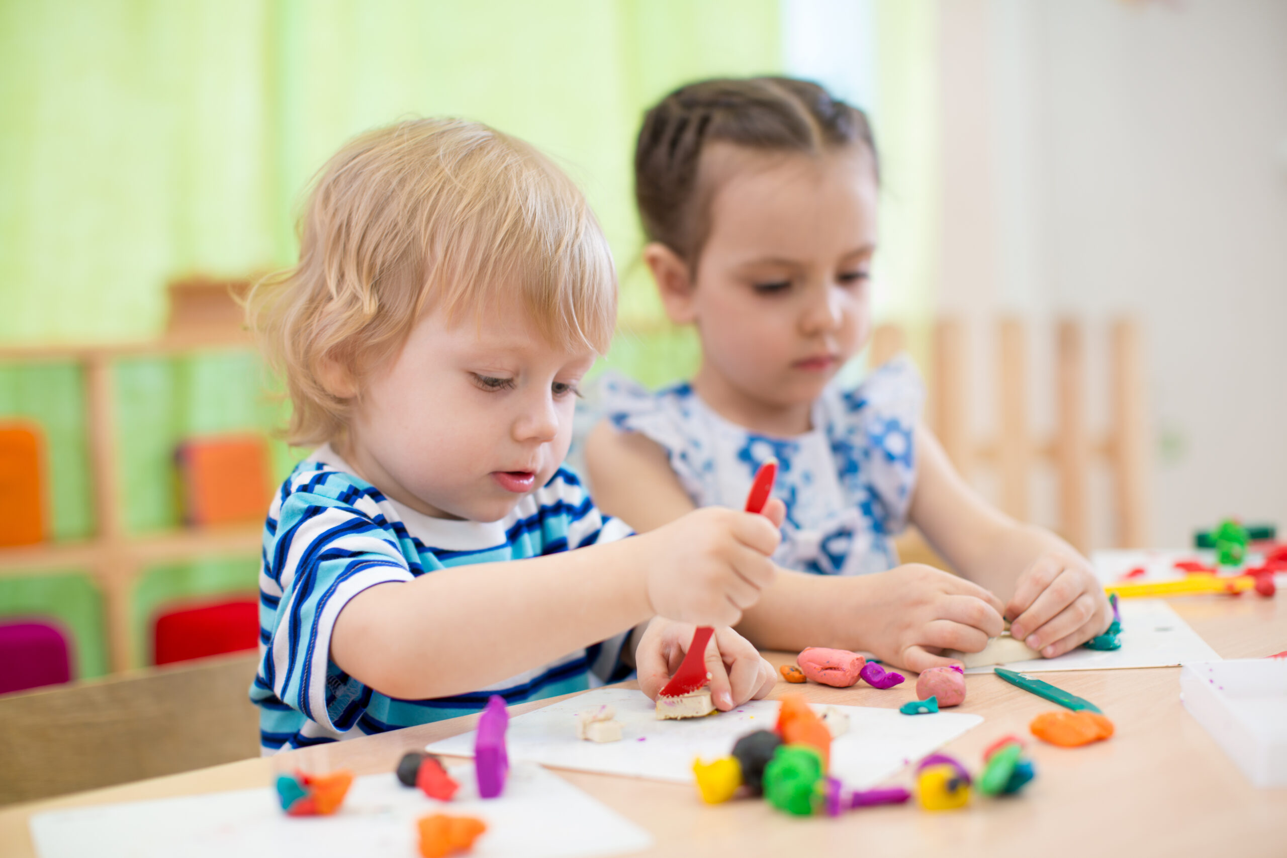 two toddlers parallel playing, sitting next to each other playing playdough.