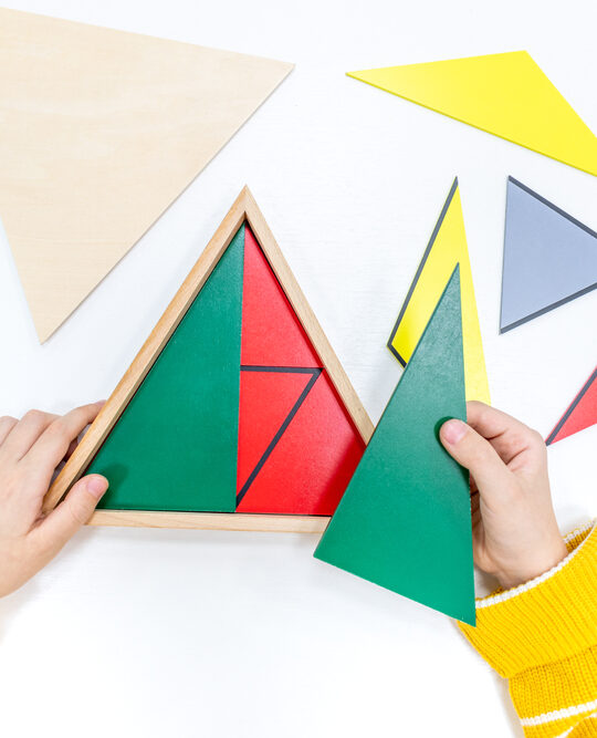 Image of child working with green, blue, anf yellow Montessori Constructive triangles.